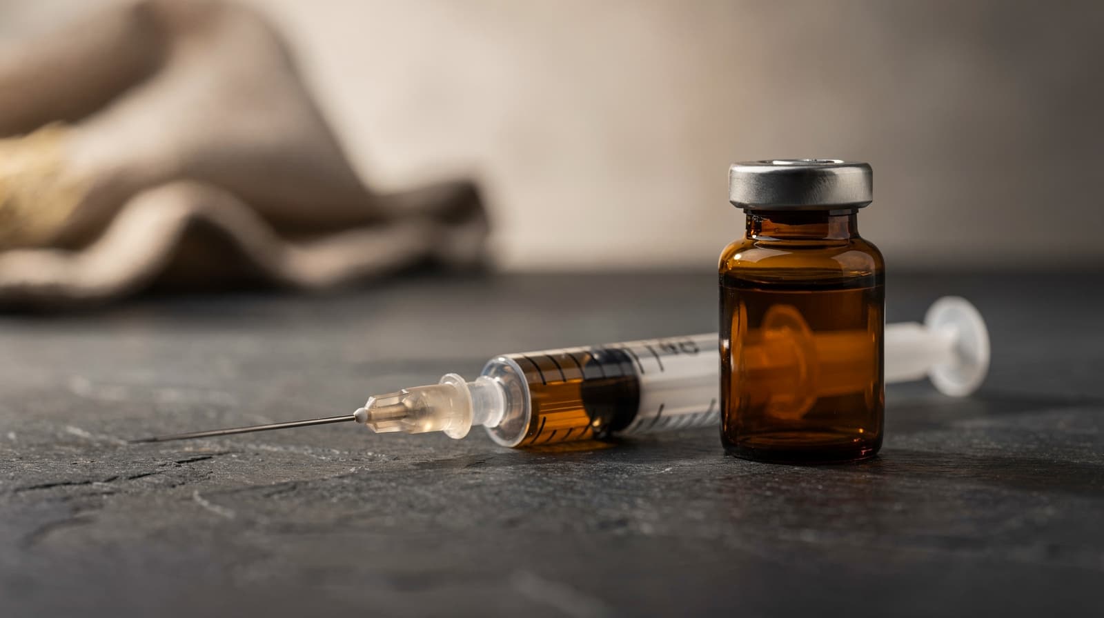 A single amber glass vial and stainless steel syringe on a dark slate counter under soft side light, researching peptides for inflammation